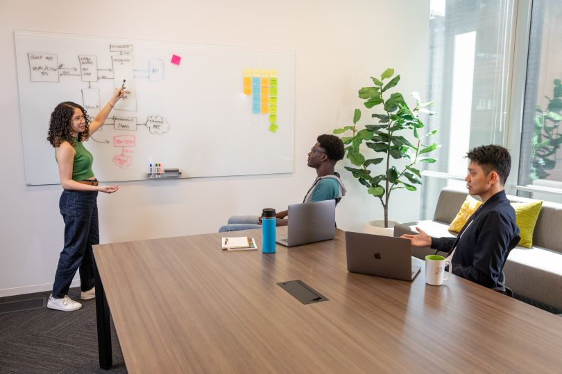 sprout social team member presenting on a whiteboard to two sprout social team members sitting at a table